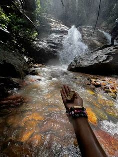 a hand reaching out to a waterfall in the woods