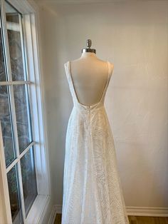 a white dress on display in front of a window with a wooden floor and windowsill