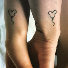 two people with mickey mouse tattoos on their arms and legs, both holding hands together