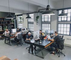 several people sitting at desks in an office setting with computers and other items on the tables