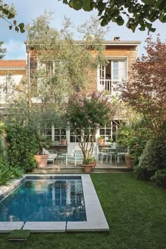 a small pool in the middle of a lawn with chairs around it and trees on either side