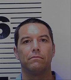 a man is looking at the camera while wearing a blue shirt and standing in front of a white wall