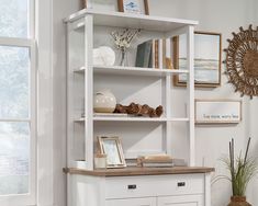 a white book shelf with books and pictures on it next to a potted plant