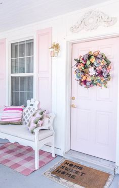 a white bench sitting in front of a pink door with a wreath on top of it