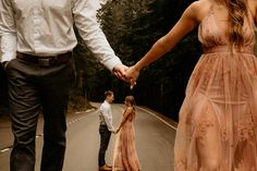 a man and woman holding hands while walking down the road