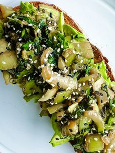 a white plate topped with a sandwich covered in veggies and sesame seed seeds