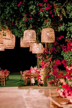 an outdoor dining area with pink flowers and hanging lights over the tables at night time