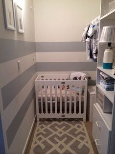 a baby's room with grey and white stripes on the walls, crib