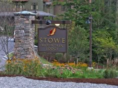 the sign for stowe mountain lodge is shown in front of some trees and flowers