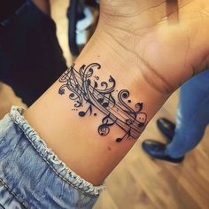 a woman's wrist tattoo with musical notes and trelliss on the band