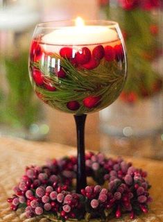 a candle that is sitting in a glass bowl with berries on the rim and greenery around it