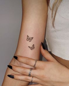 two women with matching tattoos on their arms holding each other's hands and one has a butterfly tattoo on her left arm