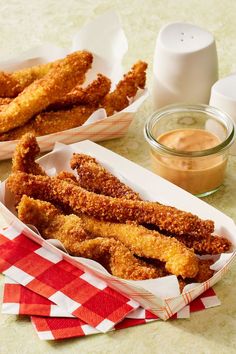 two baskets filled with fried food sitting on top of a table next to dipping sauce