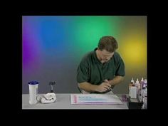 a man sitting at a table writing in front of an assortment of pens and markers