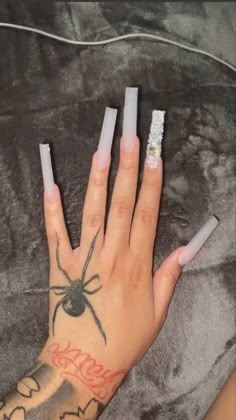 a woman's hand with white nail polish and a spider tattoo on her arm