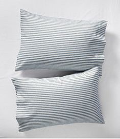 two pillows sitting next to each other on top of a white bedding set with blue stripes