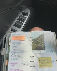 a car dashboard with a note book in the passenger seat and a hand holding a pen