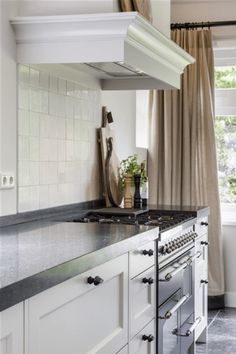 a stove top oven sitting inside of a kitchen next to a window with curtains on it