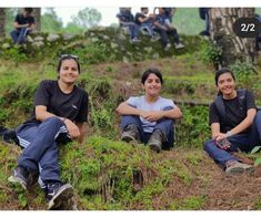 three people sitting on the ground with trees in the background