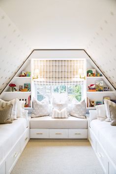 a bedroom with two white beds sitting under a window next to a shelf filled with books