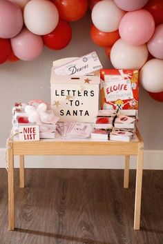 a wooden table topped with lots of balloons and boxes filled with letters to santa written on it