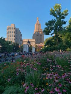 people are walking around in the city with tall buildings behind them and flowers growing on the ground