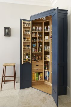 an open pantry cabinet in the corner of a room next to a stool and table