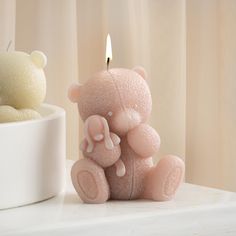 a pink teddy bear sitting next to a candle