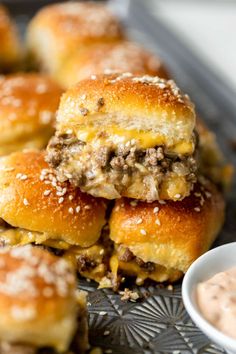 several sliders stacked on top of each other next to a small bowl of dip