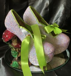 two pairs of shoes with green bows on top of each other, sitting on a glass plate