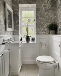 a white toilet sitting under a window next to a sink and radiator in a bathroom