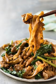 someone is holding chopsticks over a plate of stir fried noodles with mushrooms and spinach