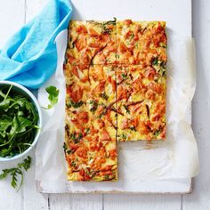 a white plate topped with slices of pizza next to a bowl of greens and a blue napkin