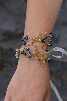 a woman's hand wearing a bracelet with blue beads and gold leaves on it