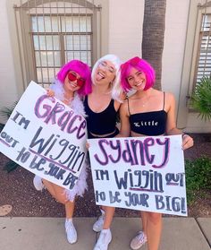 three women holding up signs in front of a building with palm trees and bushes behind them