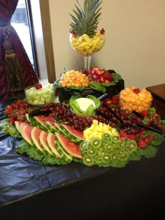 a table topped with fruits and vegetables on top of a black cloth covered table next to a window