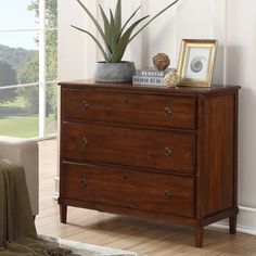 a wooden dresser with two pictures and a potted plant sitting on top of it