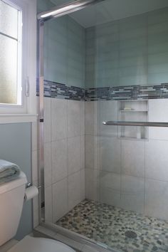 a white toilet sitting next to a walk in shower under a bathroom window on top of a tiled floor