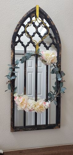 a mirror hanging on the wall with flowers in front of it and a door behind it