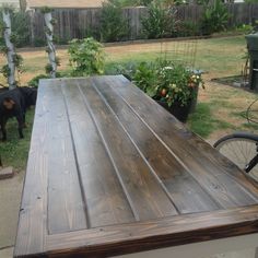 a black dog standing next to a wooden table in the yard with potted plants