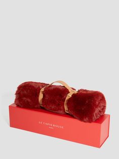 a pair of red fur cuffs sitting on top of a red box with a leather strap