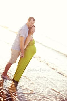 a pregnant couple standing in the water at the beach