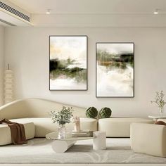 two paintings hang on the wall above a white couch and coffee table in a living room