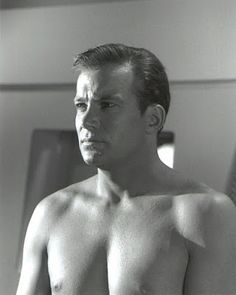 black and white photograph of a man with no shirt looking at something in the mirror