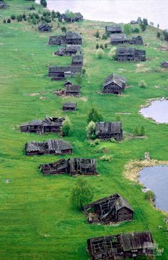 an aerial view of old wooden houses on the side of a grassy hill next to a body of water