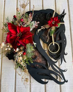 a christmas wreath with red flowers and greenery on a white wooden surface, surrounded by scissors