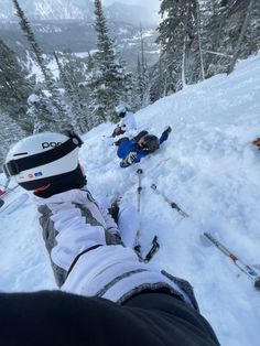 skiers and snowboarders on the side of a snowy mountain with trees in the background