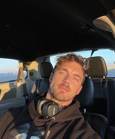 a man sitting in the passenger seat of a car looking out at the ocean and mountains