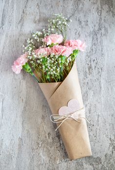 a bouquet of pink roses wrapped in brown paper with a heart shaped tag on it