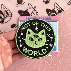 a hand holding a patch that says, not of this world